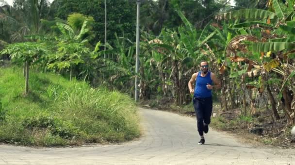 Hombre corriendo en el camino en el parque tropical — Vídeo de stock