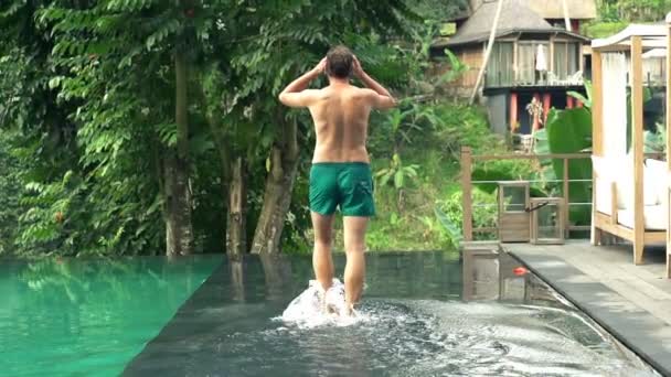 Мужчина ходит по краю бассейна и вытягивает руки — стоковое видео