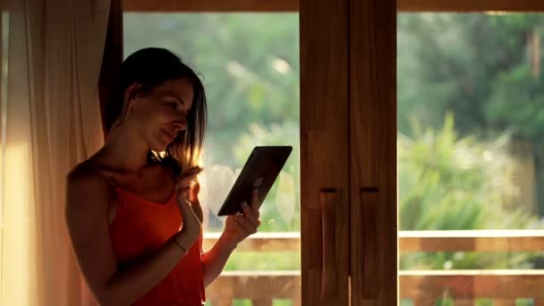 Kobieta za pomocą tabletu komputer stojący przez okno — Wideo stockowe