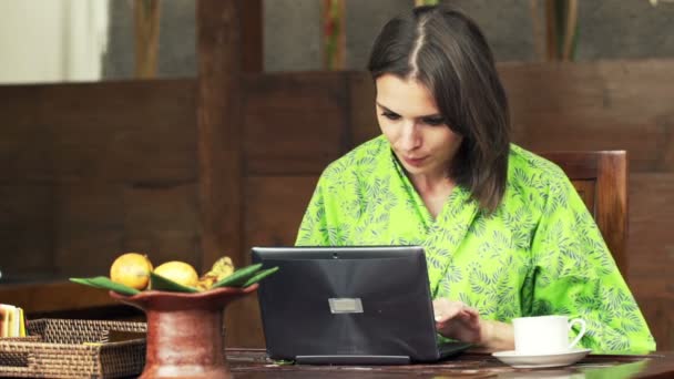 Mujer usando el ordenador portátil por mesa en la cocina — Vídeos de Stock