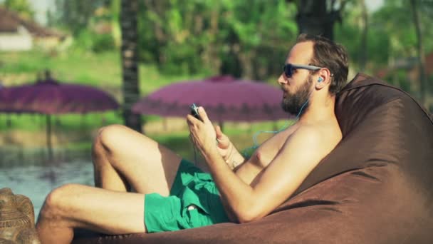 Muž, opalování, poslouchat hudbu a relaxaci u bazénu — Stock video