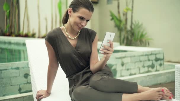 Elegant kvinna textning på smart telefon sitter på solarium — Stockvideo
