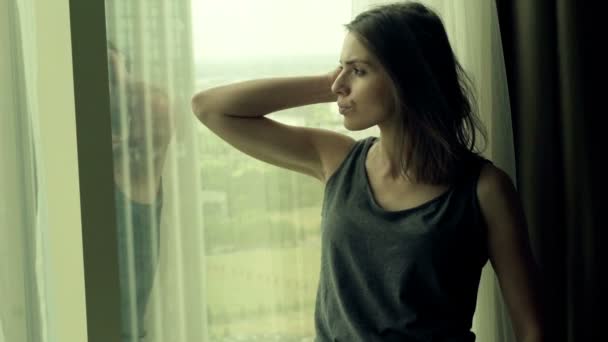 Mujer triste de pie junto a la ventana en casa — Vídeos de Stock