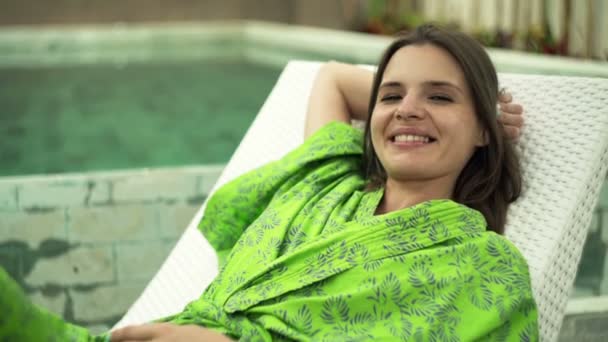 Femme parlant à la caméra sur un transat près de la piscine — Video