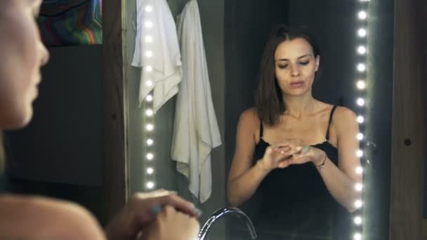 Женщина наносит увлажняющий крем на руки в ванной комнате — стоковое видео