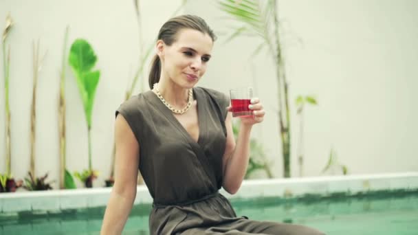 Frau trinkt Getränk sitzend am Pool — Stockvideo