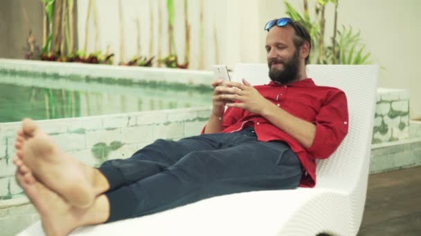 Hombre mensajes de texto en el teléfono inteligente tumbado en la cama solar — Vídeos de Stock