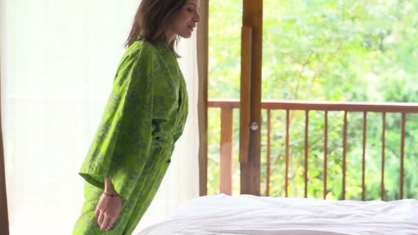 Молодая женщина в халате падает на кровать — стоковое видео