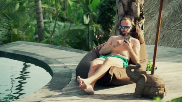 Człowiek z smartphone leżącego na worek fasoli — Wideo stockowe