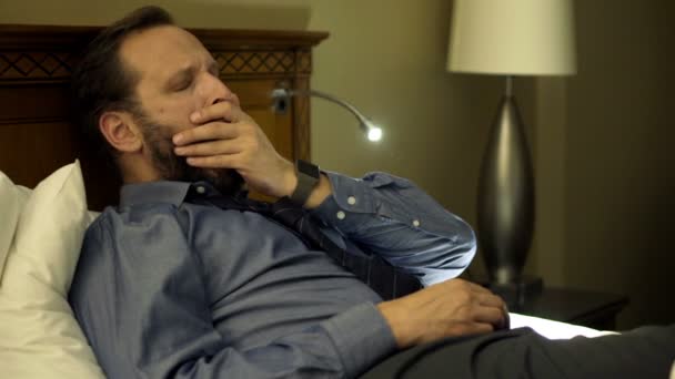 Бізнесмен позіхає і засинає на ліжку — стокове відео