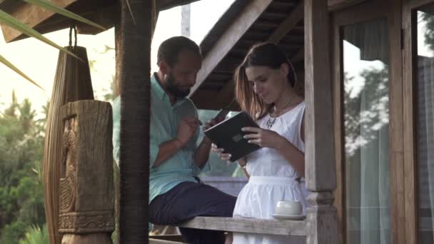 Пара с помощью смартфона и планшетного компьютера на террасе — стоковое видео