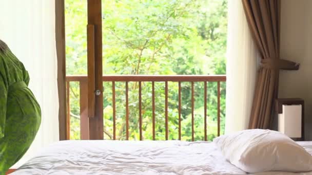 Young woman in bathrobe jumping on bed — Stock Video