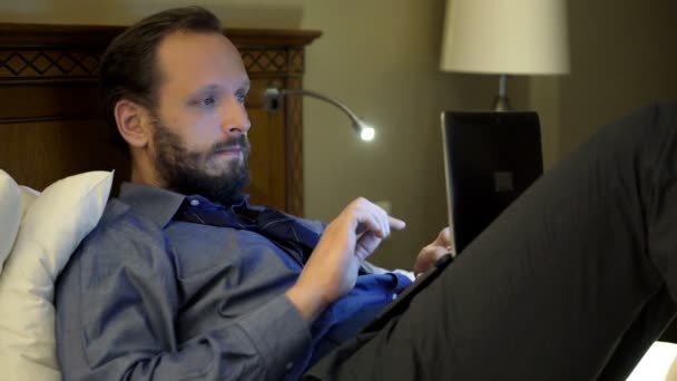 Hombre de negocios que trabaja con el ordenador portátil acostado en la cama — Vídeos de Stock