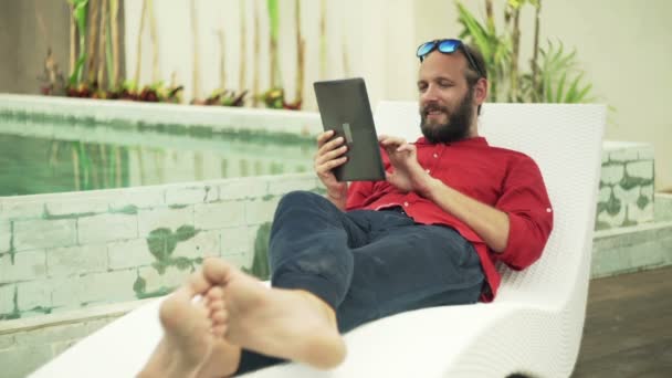 Hombre usando la tableta de ordenador en el solarium junto a la piscina — Vídeo de stock