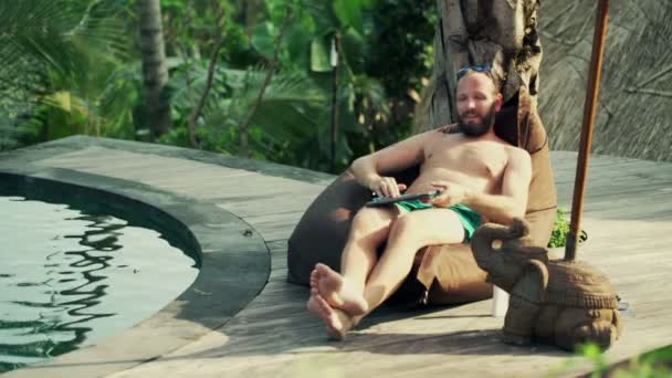 Hombre con portátil moderno relajándose junto a la piscina — Vídeos de Stock