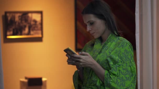 Mujer usando smartphone por ventana en casa — Vídeos de Stock