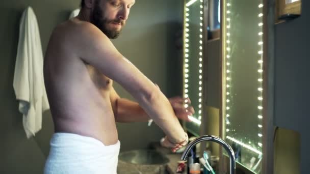Мужчина наносит увлажняющий крем на руку и руки в ванной комнате — стоковое видео