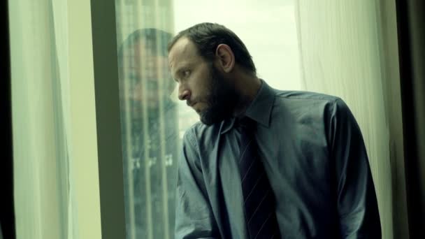 Sad, unhappy businessman sitting by window — Stock Video