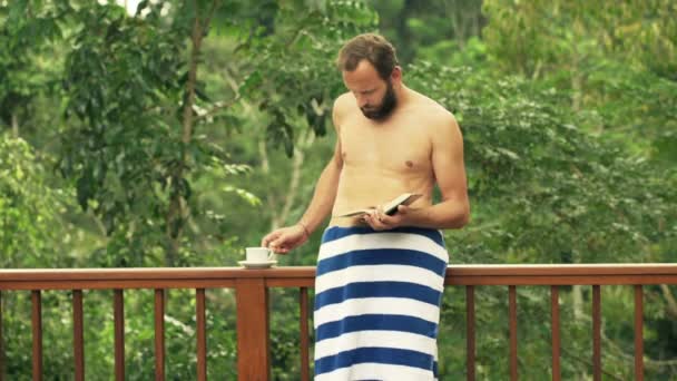 Człowiek, czytanie książki i picie kawy na tarasie — Wideo stockowe