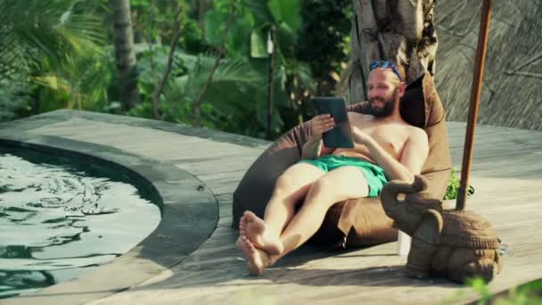 Homem com computador tablet relaxante junto à piscina — Vídeo de Stock