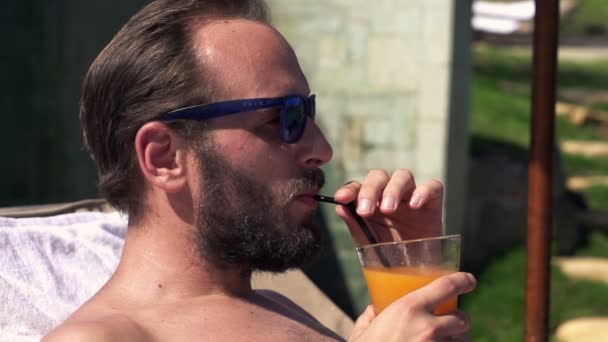 Человек загорает и пьет коктейль в саду — стоковое видео