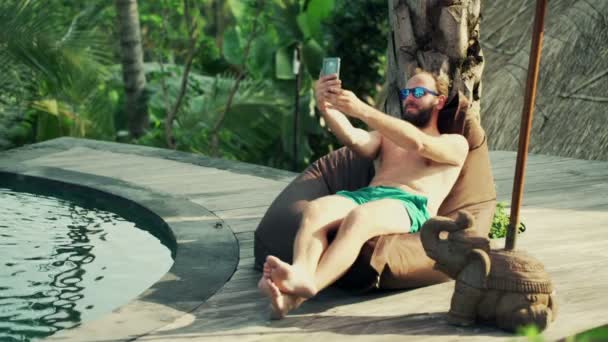 Мужчина делает селфи фото со смартфоном у бассейна — стоковое видео