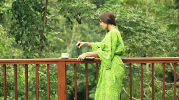 Mujer usando el ordenador portátil moderno y beber café en la terraza — Vídeo de stock