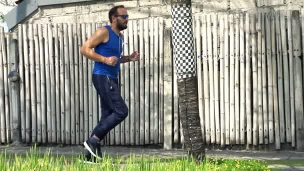 Młody człowiek jogging w kraju w pobliżu ogrodzenia — Wideo stockowe