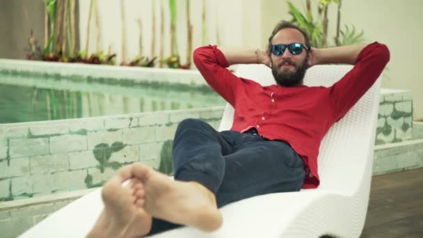 Hombre hablando acostado en la cama de sol junto a la piscina — Vídeos de Stock