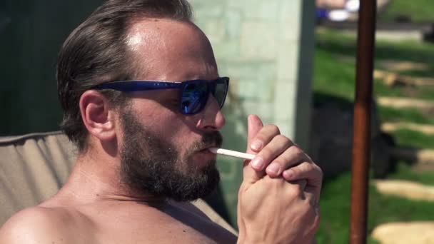 Man roken sigaret tijdens het zonnebaden in de tuin — Stockvideo