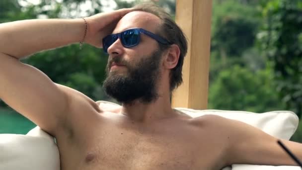 Man relaxing on sunbed by swimming pool — Stock Video