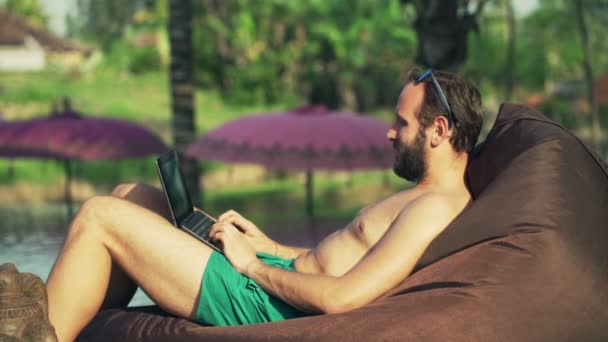 Uomo che utilizza il computer portatile mentre si rilassa in piscina — Video Stock