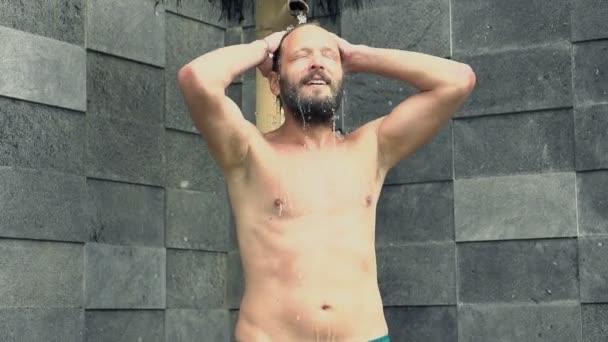 Человек моет свое тело под открытым душем — стоковое видео