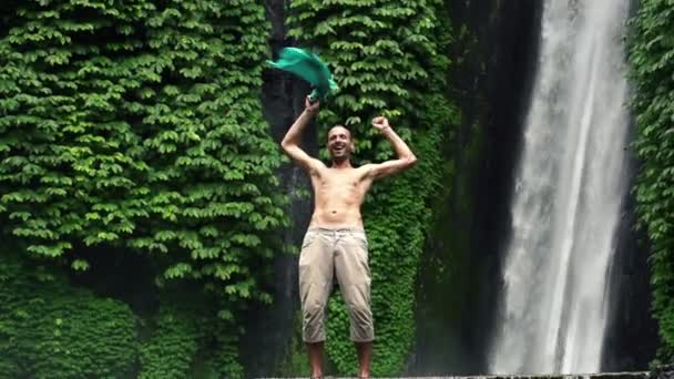 Emocionado hombre agitando camiseta por cascada — Vídeos de Stock