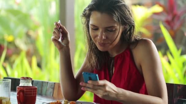 Mujer mensajes de texto en el teléfono inteligente y comer — Vídeos de Stock