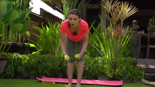 Женщина упражняется с гантелями в саду — стоковое видео
