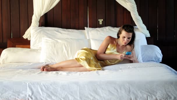 Женщина пишет смс на смартфоне на большой кровати — стоковое видео
