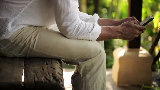 Человек, который пишет смс на смартфоне, сидит на скамейке — стоковое видео