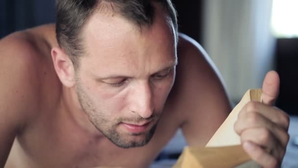 Mann liest Buch auf bequemem Bett — Stockvideo