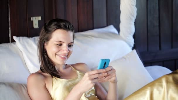 Mujer mensajes de texto en el teléfono inteligente en la cama grande — Vídeos de Stock