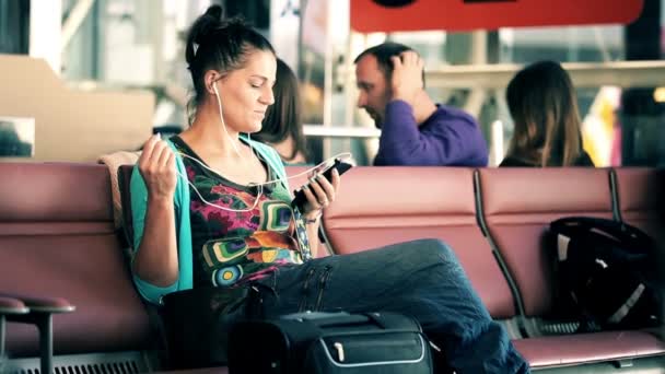 Attractive young woman listening music on smartphone at airport — Stock Video