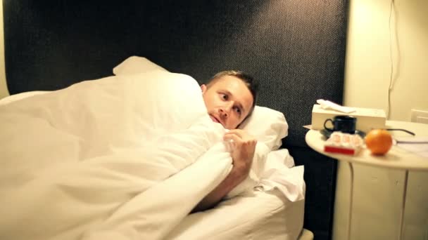 Больной человек принимает таблетки, лежит в постели поздно ночью — стоковое видео