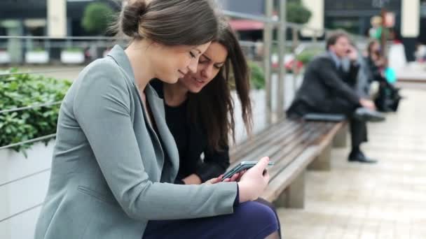 Zwei hübsche Geschäftsfrauen schauen sich etwas auf dem Smartphone an — Stockvideo