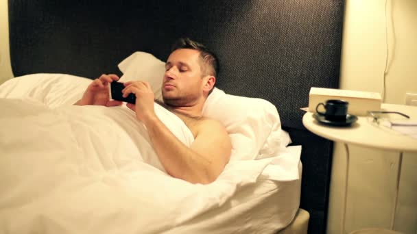 Человек со смартфоном лежит в постели поздно ночью — стоковое видео