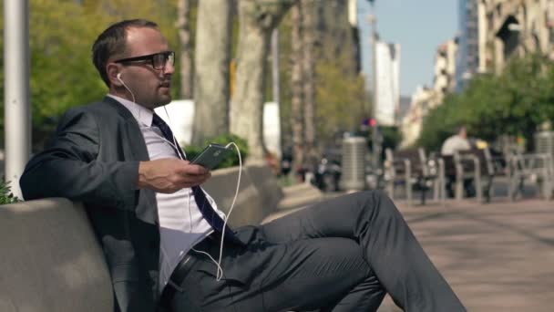 Gelukkig zakenman luisteren naar de muziek op smartphone in de stad — Stockvideo
