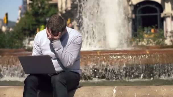 市内の噴水によってラップトップに悪いニュースを読むビジネスマン — ストック動画