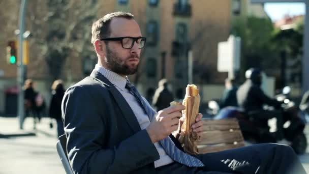 Young handsome businessman eating baguette by the city street — Stock Video