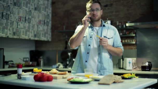 Young man talking on cellphone and eating in kitchen — Stock Video