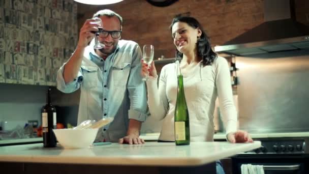 Pareja joven levantando tostadas con vino, celebrando en la cocina en casa — Vídeo de stock