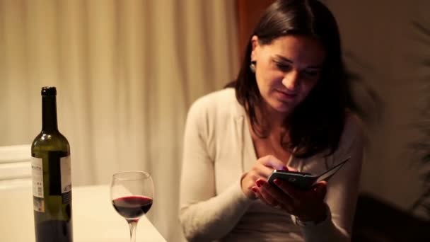 Žena textilie na smartphone a pití vína podle tabulky — Stock video